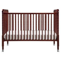 a baby crib with white sheets on the bottom, and brown wood trims