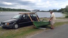 a man standing next to a green boat on the side of a road near water