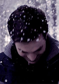 a man standing in the snow looking down at his cell phone while it's raining