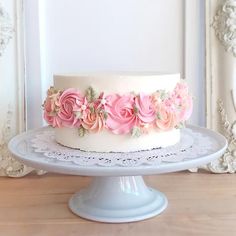 a white cake with pink flowers sitting on top of a table next to a mirror