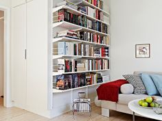 a living room filled with lots of books on top of a white book shelf next to a couch