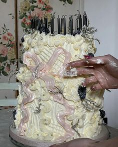 a woman is decorating a white cake with black and pink icing on it