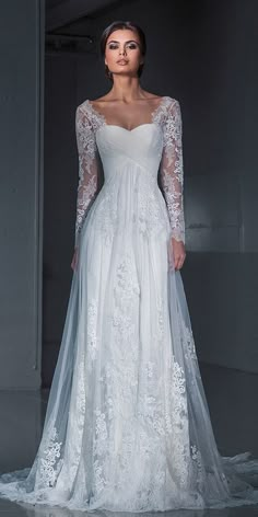 a woman in a white wedding dress with long sleeves and sheer lace on the skirt