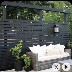 a couch and table on a patio with some plants in front of the fenced off area