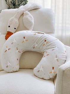 a stuffed animal sitting on top of a white chair next to a pillow and pillows