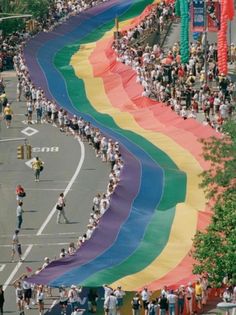 a large rainbow flag is being carried down the street