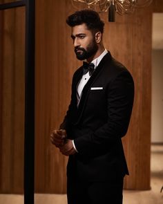 a man in a tuxedo standing next to a chandelier