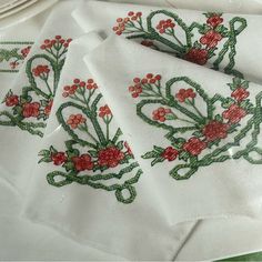 three white napkins with red flowers and green stems on them sitting on a table