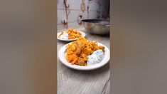 two white plates filled with food sitting on top of a wooden table next to a metal pan