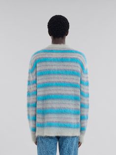 a man standing in front of a white wall wearing a blue and grey striped sweater