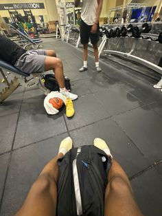 the man is laying down in the gym with his back turned to the camera while another person works out behind him