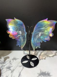 a colorful butterfly sculpture sitting on top of a metal stand next to a potted plant