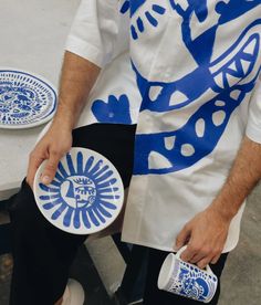 a man sitting down holding two plates with blue designs on them and one has his hand in the other's pocket