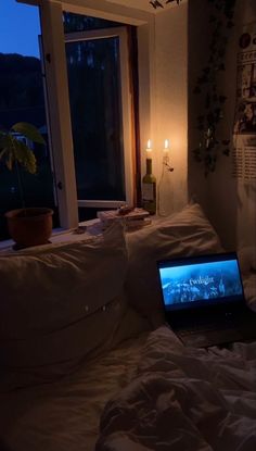 an open laptop computer sitting on top of a bed next to a window at night