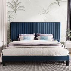 a bed with blue velvet headboard and pillows in a white room next to a window