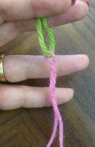 a hand holding a pink and green string on top of a wooden table next to a pair of scissors