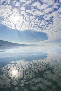 the sun shines brightly through clouds over calm water on a clear, sunny day