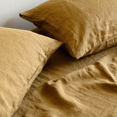 two brown pillows sitting next to each other on top of a bed covered in tan linens