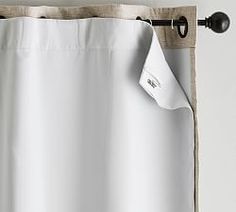 a white curtain hanging on the side of a window with an iron rod and black hardware