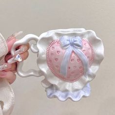 a hand holding a pink and white ceramic teapot with a bow on it's handle