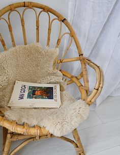 a book sitting on top of a chair next to a white curtain and window with curtains behind it