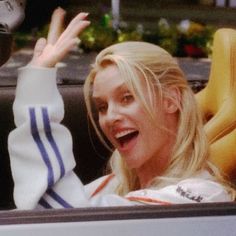 a blonde woman sitting in the back of a car waving to someone with her hand up