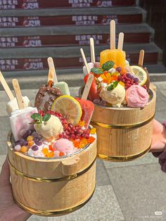 two wooden buckets filled with different types of ice cream and toppings on sticks