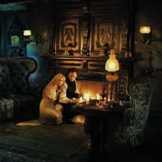 a man and woman sitting at a table in front of a fireplace with candles on it