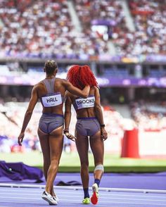 two women in bikinis standing on a track with their arms around each other and looking at the crowd