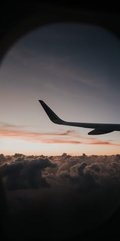 an airplane is flying in the sky above some clouds at sunset or dawn with it's wing visible