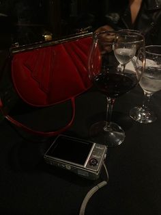 a red purse sitting on top of a table next to two wine glasses and a cell phone