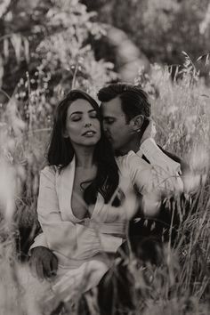 a man and woman sitting in the middle of some tall grass with their eyes close to each other