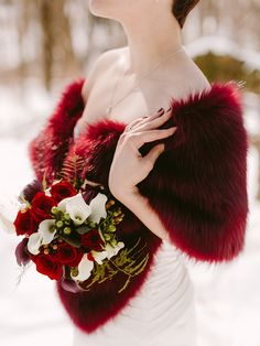 a woman in a white dress holding a red and white bouquet with fur stole around her neck