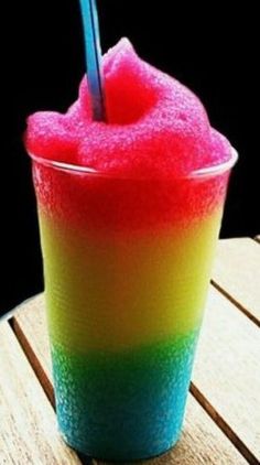 a colorful drink sitting on top of a table next to a wooden table with a straw sticking out of it