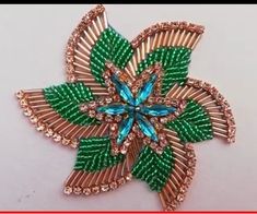 a brooch with green leaves and blue crystals on it's center, sitting on a white surface