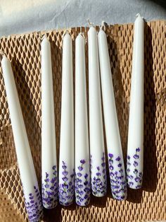 five white candles with purple flowers painted on them sitting on a woven place mat,