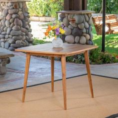 a wooden table sitting on top of a rug in front of a stone wall and bench