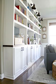 a living room filled with lots of white bookshelves next to a gray couch