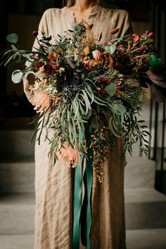 a woman holding a large bouquet of flowers and greenery in her hands while standing on steps