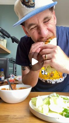 a man sitting at a table in front of a bowl of salad eating a sandwich