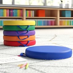 a stack of colorful plastic discs sitting on top of a white floor next to a bookshelf