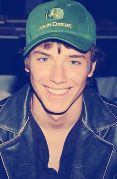 a black and white photo of a young man wearing a john deere hat smiling