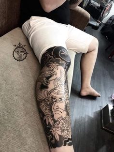 a person with a tattoo on their leg sitting on a couch and holding a cell phone