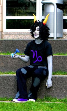 a man with horns and makeup sitting on the steps wearing a costume that has scissors in his hand