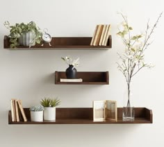 two wooden shelves with books, vases and plants on them against a white wall