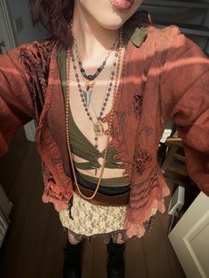 a woman with red lipstick and necklaces standing in front of a mirror wearing an orange shirt