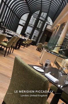 the interior of a restaurant with wooden floors and glass walls, along with green chairs