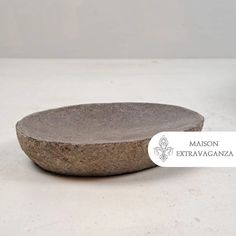 a stone bowl sitting on top of a white table next to a planter with a label that says maison extrananza