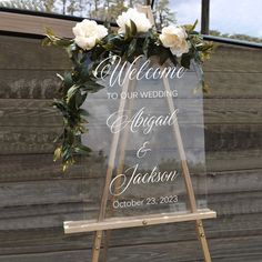 a clear acrylic sign that says welcome to our wedding with flowers on it