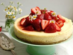 a cheesecake topped with fresh strawberries and daisies on a green cake plate